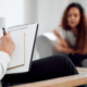 Mujer de fondo, platicando con su médico, mientras él toma notad